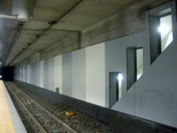 From the northbound platform, the escalators to the southbound platform below can be seen through windows. The platform boxes are one above the other, but the platforms need to be accessed separately due to the one-sided trams