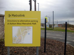 Sign with directions to Ashton West car park at car park exit with station in background