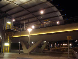 Looking at the station from the side of the street with the Metrolink logo sign in view. The stairs and lift to the platform for trams to Manchester are on the left